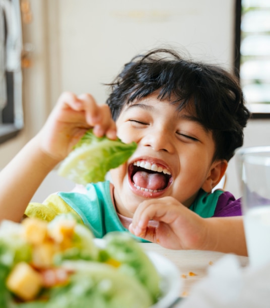 Kid eating a piece of lettuce and laughing