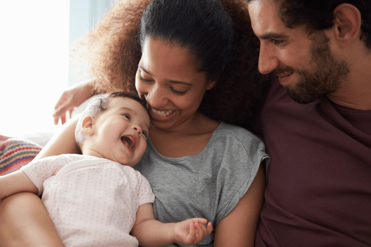 Young mother and father holding smiling baby with mouth wide open