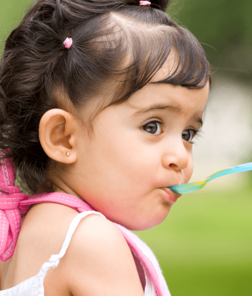 Young girl eating from teal spoon in public park