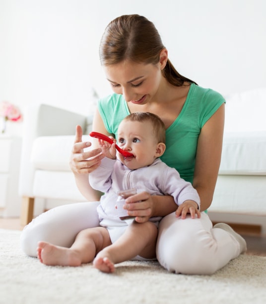 Mother sitting on carpet spoon feeding her child