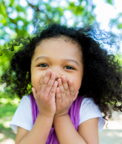 Young girl with hands over mouth to cover laughter in public park
