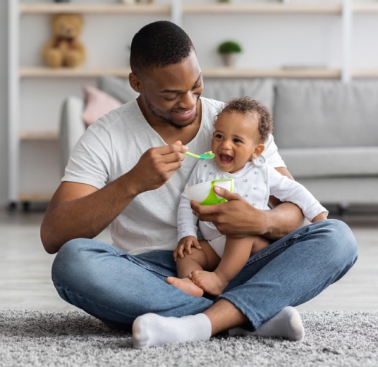 Father sitting on carpet spoon feeding baby