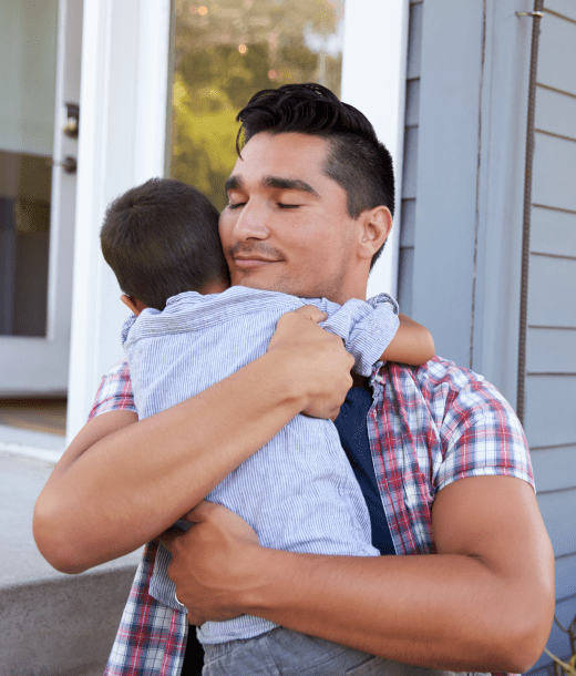 Father in checked shirt embracing baby outside of house