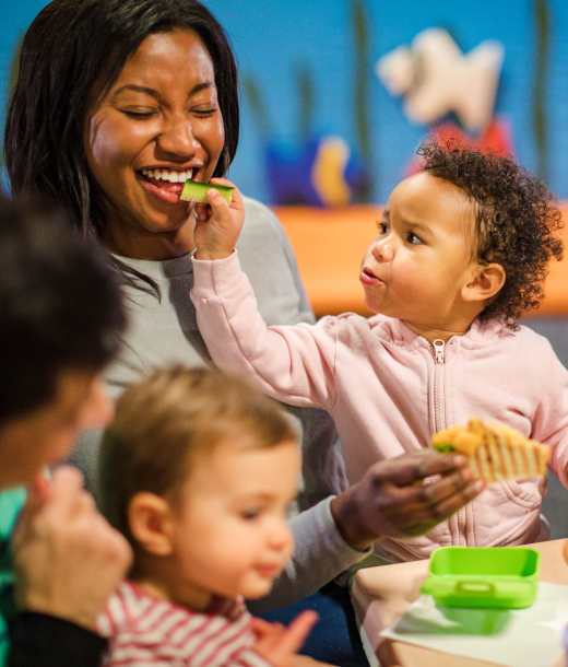 Baby at community center feeding mother a cucumber as she laughs