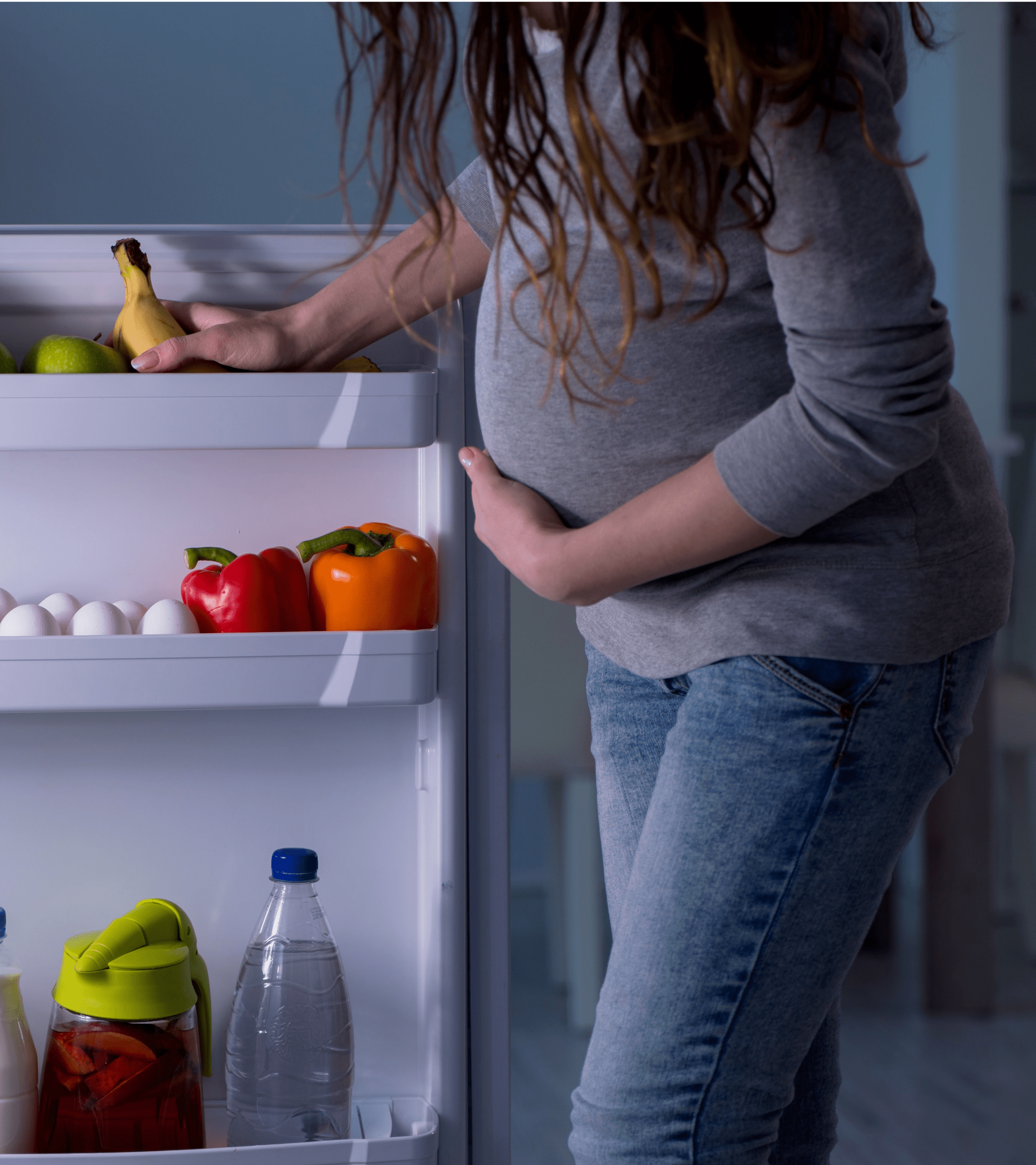 Pregnant woman looking for healthy food inside the refrigerator